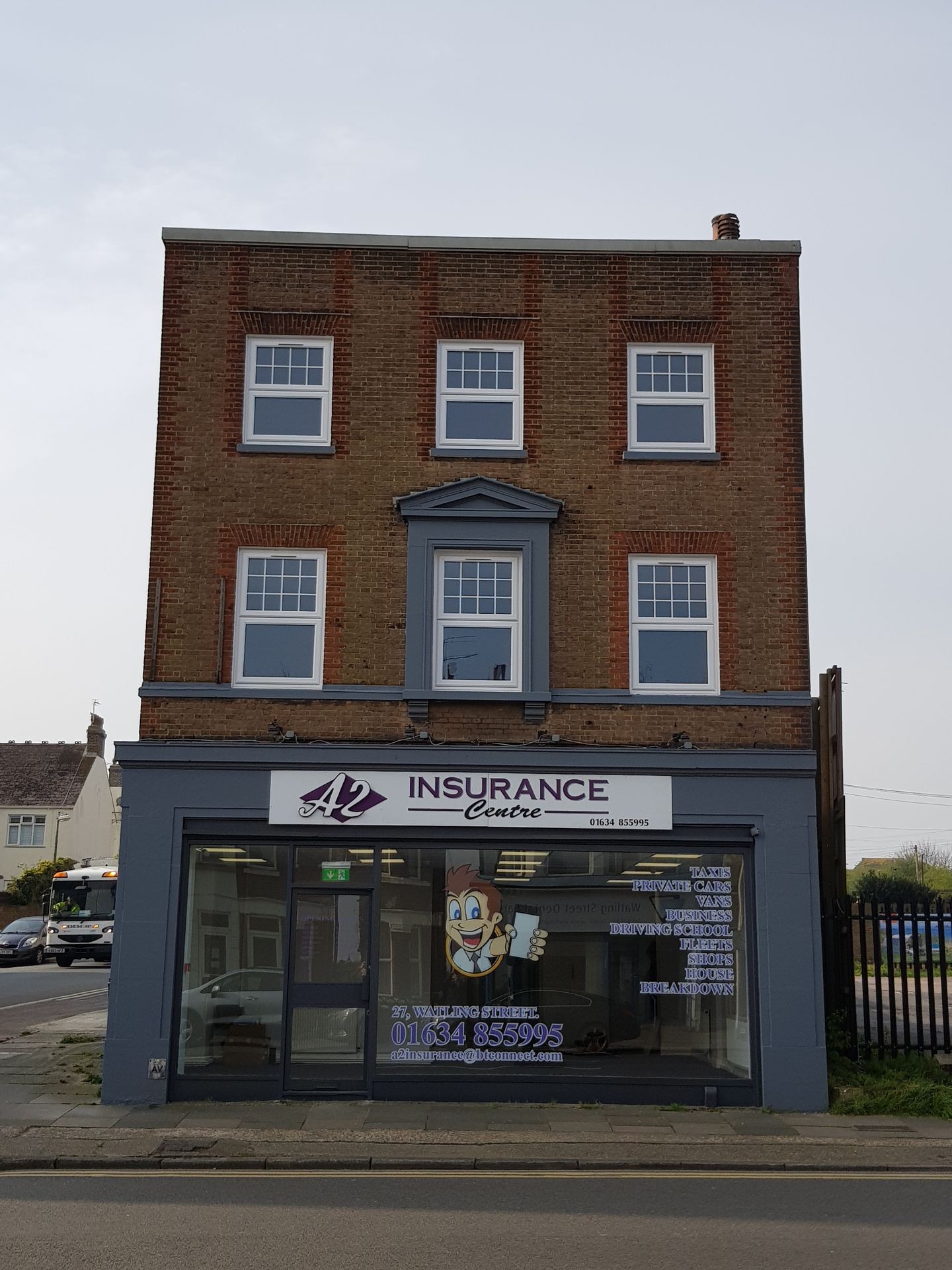 Exterior view of a multi-story insurance office building with large windows on the ground floor displaying advertisements.